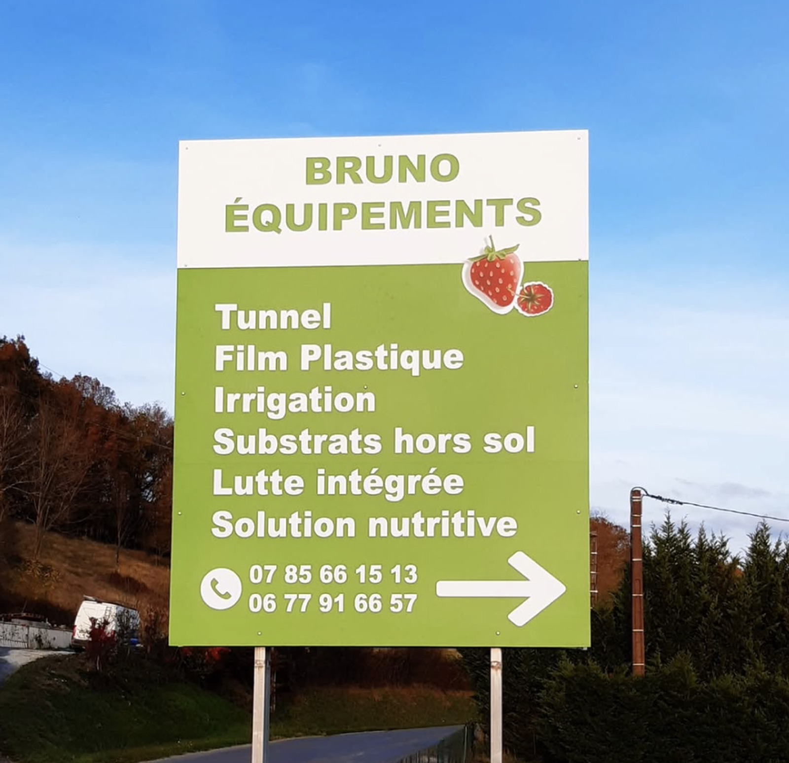 Panneau d'entrée Bruno Équipements listant les activités (tunnel, film plastique, irrigation, substrats hors sol, lutte intégrée, solution nutritive) ; des numéros de téléphone y sont lisibles — BRUNO EQUIPEMENT